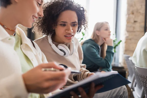 Lächelnder Student zeigt entmutigten afrikanisch-amerikanischen Freund Notizbuch — Stockfoto