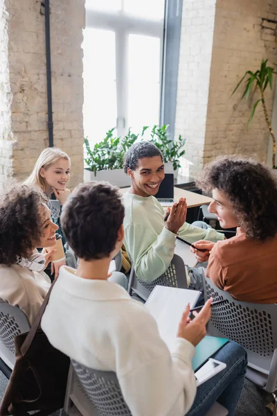 Junge multikulturelle Studenten sitzen im Klassenzimmer und lächeln während des Gesprächs — Stockfoto