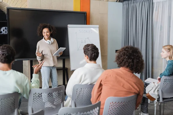 Mulher africana americana com tablet digital perto whiteboard com tarefa e estudantes inter-raciais em sala de aula — Fotografia de Stock