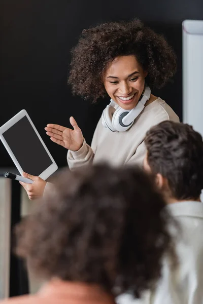 Sorrindo estudante afro-americano com fones de ouvido mostrando tablet digital para colega turvo — Fotografia de Stock