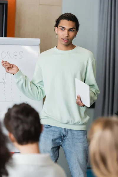 African american student with digital tablet talking to blurred classmates near whiteboard with task — Stock Photo