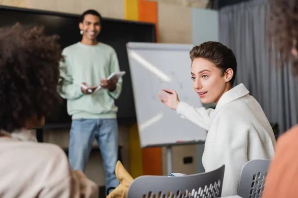 Sonriente mujer apuntando a africano americano estudiante de pie cerca borrosa pizarra blanca - foto de stock