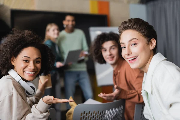 Estudiantes multiétnicos felices mirando a la cámara cerca de compañeros de clase en un fondo borroso - foto de stock