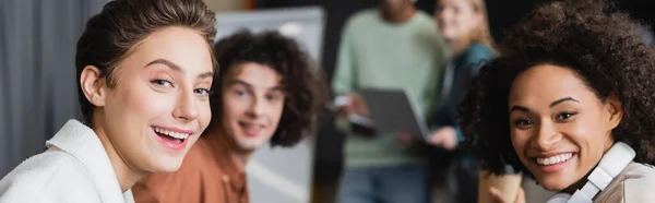 Estudiantes multiculturales alegres mirando a la cámara sobre fondo borroso, pancarta - foto de stock