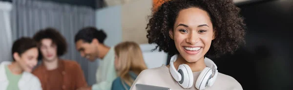 Joven afroamericano estudiante con auriculares mirando a la cámara en un fondo borroso, pancarta - foto de stock