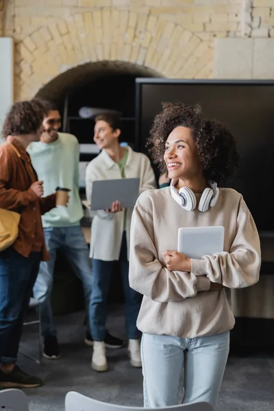 Glückliche afrikanisch-amerikanische Frau mit digitalem Tablet in der Nähe von interrassischen Studenten, die auf verschwommenem Hintergrund sprechen — Stockfoto