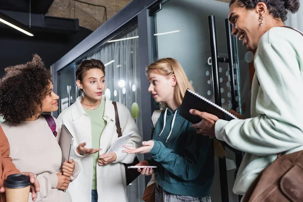 Young women talking and gesturing near african american friends in university — Stock Photo