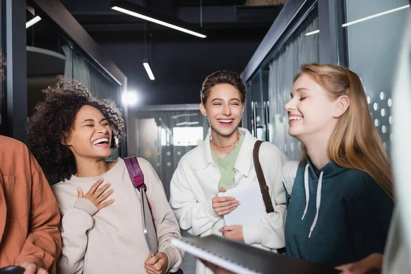 Aufgeregte afrikanisch-amerikanische Frau lacht und berührt Brust in der Nähe von Freunden in der Universität — Stockfoto