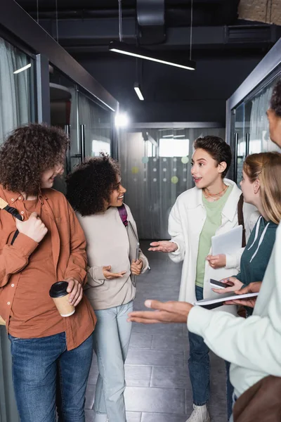 Étudiants interraciaux joyeux geste tout en parlant dans le couloir de l'université — Photo de stock