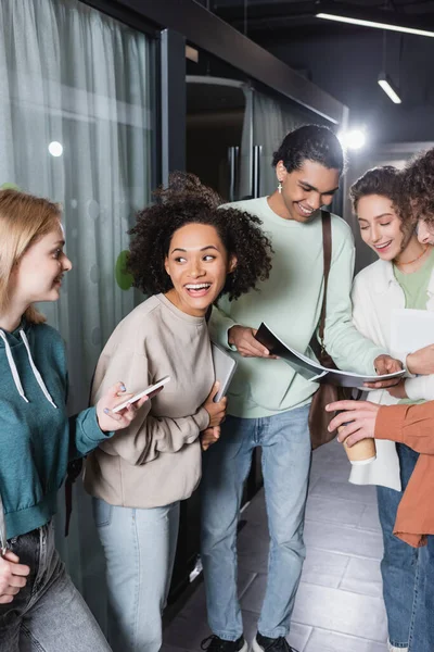 Estudiante afroamericano mostrando copybook a compañeros de clase multiculturales alegres - foto de stock