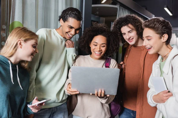 Happy african american woman holding laptop near smiling multiethnic friends — Stock Photo