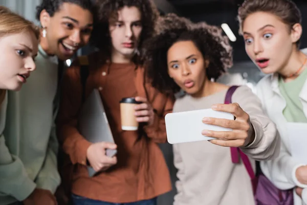 African american woman pouting lips while showing smartphone to amazed multiethnic  friends — Stock Photo