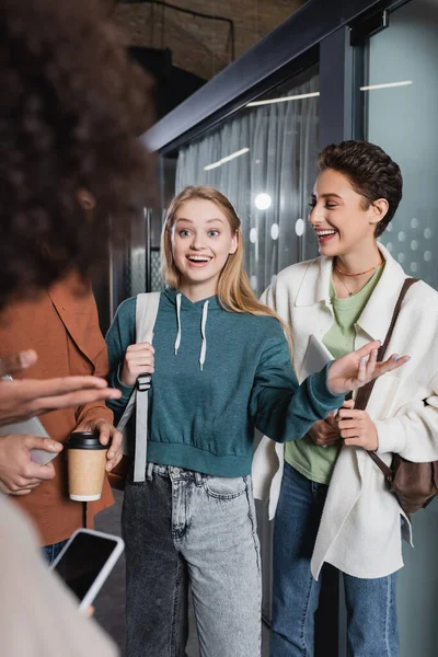 Smiling woman pointing with hand while talking to multicultural students in university — Stock Photo