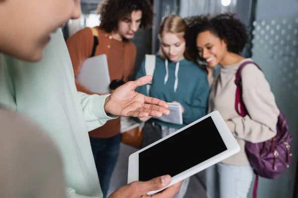 Africano americano hombre apuntando con la mano en digital tablet con blanco pantalla cerca borrosa interracial estudiantes - foto de stock