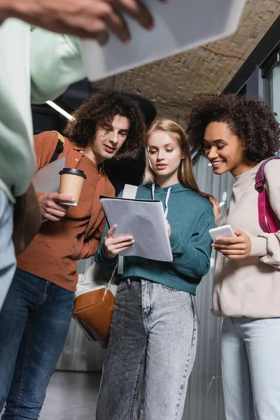 Low angle view of multiethnic students looking at copybook on blurred foreground — Stock Photo