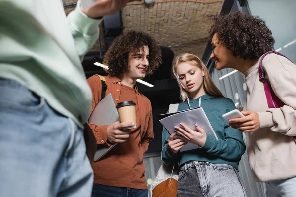 Vista de ángulo bajo de los estudiantes multiétnicos con gadgets, café para llevar y portátil - foto de stock