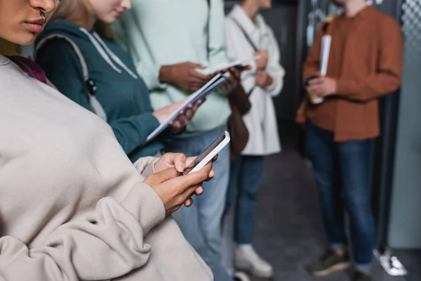 Cropped view of african american student using smartphone near blurred classmates — Stock Photo