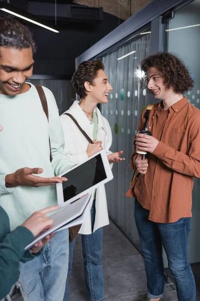 Estudiante afroamericano sonriente apuntando a la tableta digital cerca de amigos en la universidad - foto de stock