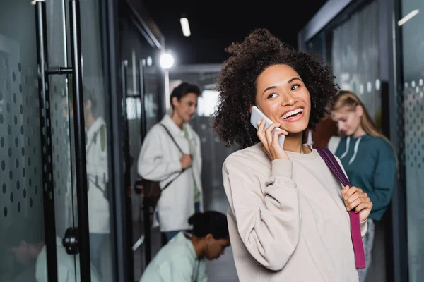 Allegra donna afroamericana che parla sul cellulare vicino ai compagni di classe su sfondo sfocato — Foto stock