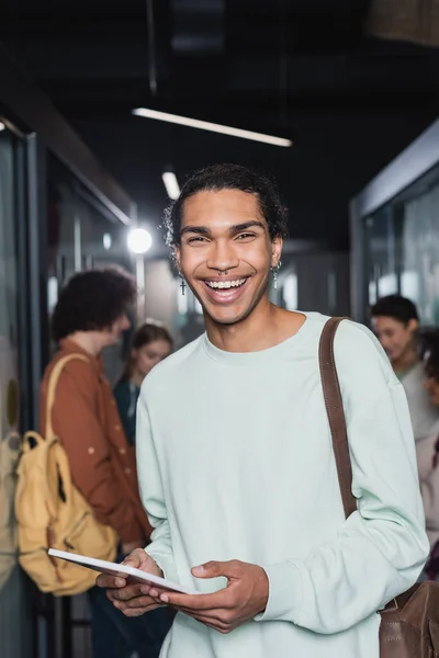 Happy and stylish african american student holding digital tablet near people on blurred background — Stock Photo