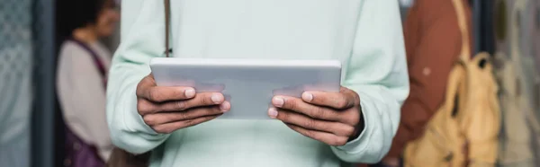 Vue partielle d'un étudiant afro-américain tenant une tablette numérique sur fond flou, bannière — Photo de stock