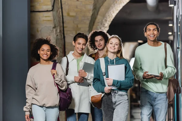 Grupo de estudiantes multiétnicos felices con mochilas y gadgets en la universidad - foto de stock