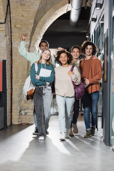 Excité étudiant afro-américain montrant geste de triomphe près de camarades de classe multiethniques dans le couloir — Photo de stock