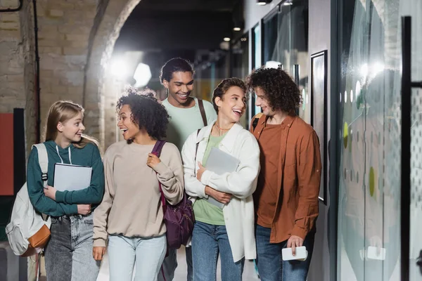 Allegro interrazziale studenti con zaini sorridenti a vicenda in corridoio di università — Foto stock