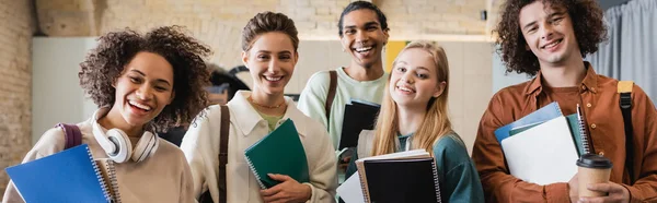 Giovani e allegri studenti multietnici con copybook sorridenti alla macchina fotografica, striscione — Foto stock