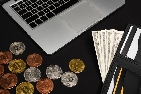 QUIIV, UCRÂNIA - 26 de abril de 2022: Vista superior da carteira com dinheiro perto de laptop e bitcoins em fundo preto — Fotografia de Stock