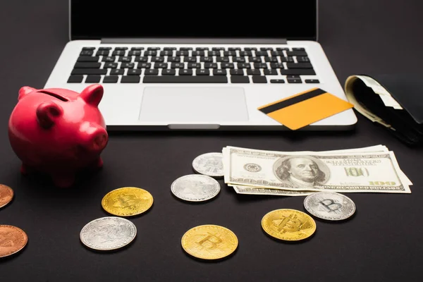 KYIV, UKRAINE - APRIL 26, 2022: Bitcoins near dollars and laptop on black background — Stock Photo