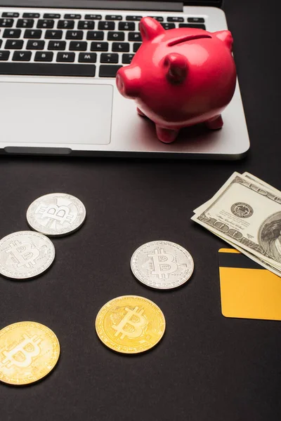 KIEW, UKRAINE - 26. April 2022: Hochwinkelaufnahme von Bitcoins in Dollar-Nähe und verschwommenem Laptop auf schwarzem Hintergrund — Stockfoto