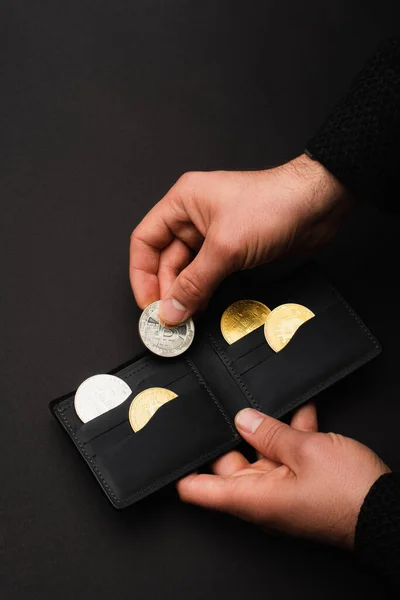 KYIV, UKRAINE - APRIL 26, 2022: Cropped view of man holding wallet with bitcoins isolated on black — Stock Photo