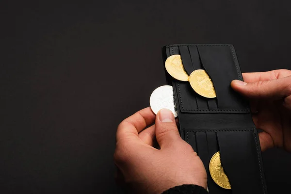 KYIV, UKRAINE - APRIL 26, 2022: Покритий погляд на людину, що тримає гаманець з різними біткоїнами, ізольованими на чорному. — стокове фото