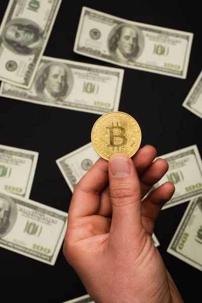 KYIV, UKRAINE - APRIL 26, 2022: Top view of man holding crypto coin near $banknotes on black background — стокове фото