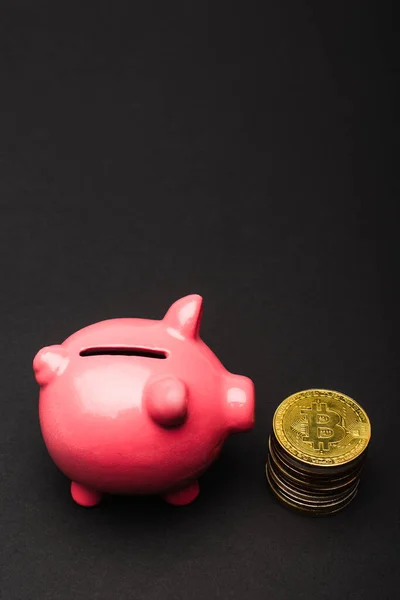 QUIIV, UCRÂNIA - 26 de abril de 2022: Vista de perto do banco piggy rosa perto de bitcoins em fundo preto — Fotografia de Stock