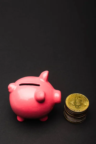 KIEW, UKRAINE - 26. April 2022: Nahaufnahme eines rosafarbenen Sparschweins in der Nähe von Bitcoins auf schwarzem Hintergrund — Stockfoto