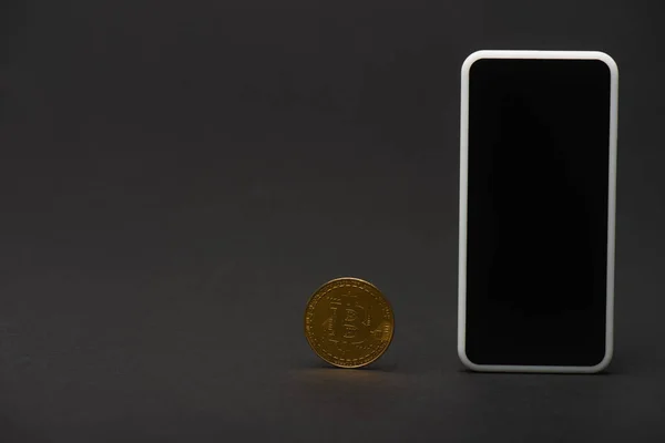 QUIIV, UCRÂNIA - 26 de abril de 2022: Bitcoin dourado e celular com tela em branco no fundo preto — Fotografia de Stock