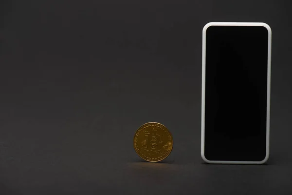 KIEW, UKRAINE - 26. April 2022: Goldener Bitcoin und Handy mit leerem Bildschirm auf schwarzem Hintergrund — Stockfoto