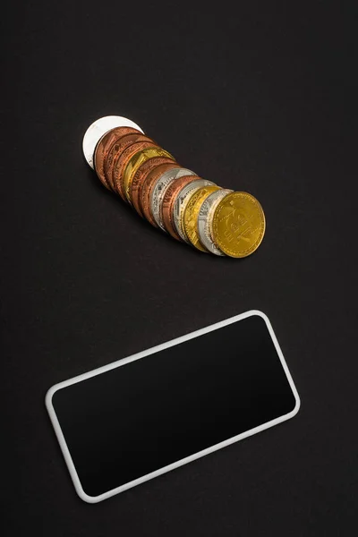 KYIV, UKRAINE - APRIL 26, 2022: Top view of mobile phone near bitcoins on black background — Stock Photo