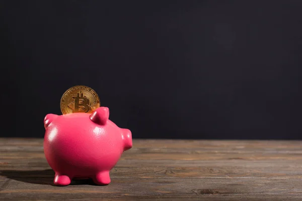 KYIV, UKRAINE - APRIL 26, 2022: Golden bitcoin on piggy bank on wooden surface on black background — Stock Photo