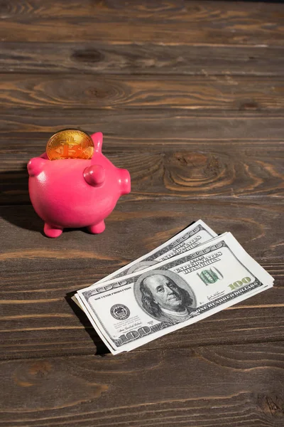 KYIV, UKRAINE - APRIL 26, 2022: High angle view of dollars near piggy bank with bitcoin on wooden surface — Stock Photo