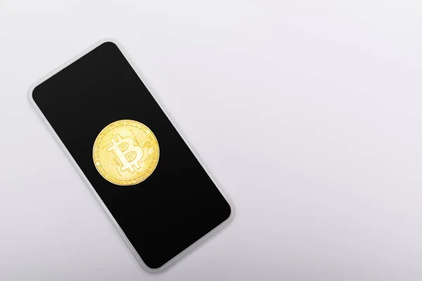 KYIV, UKRAINE - APRIL 26, 2022: Top view of golden bitcoin on smartphone on grey background — Stock Photo