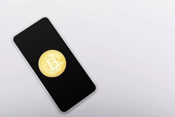 KYIV, UKRAINE - APRIL 26, 2022: Top view of gold bitcoin on smartphone on grey background — стокове фото