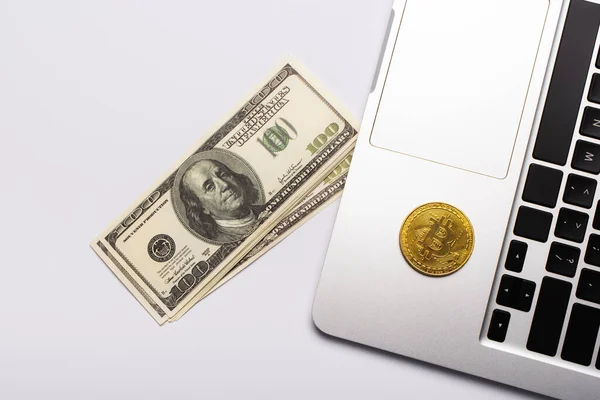 KYIV, UKRAINE - APRIL 26, 2022: Top view of dollars near bitcoin on laptop on white background — Stock Photo