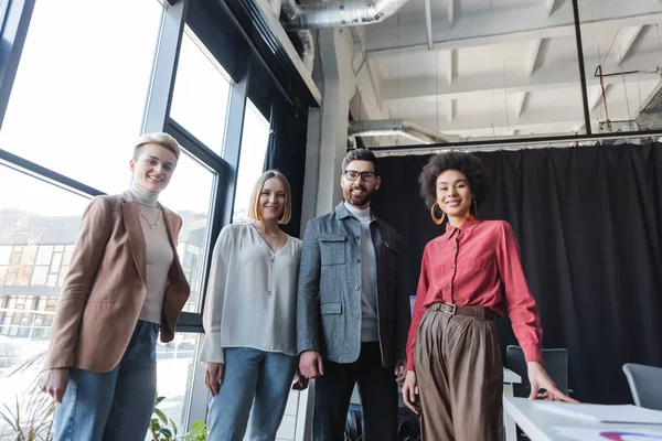 Low angle view of successful interracial business people looking at camera in advertising agency — Stock Photo