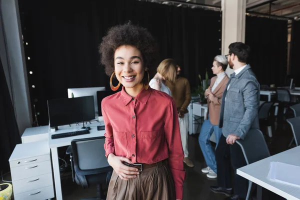 Glücklich afrikanisch-amerikanischer Werbemanager blickt in die Kamera neben verschwommenen multikulturellen Kollegen — Stockfoto