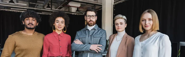 Equipo de negocios multiétnicos en ropa casual mirando a la cámara en la agencia de publicidad, pancarta - foto de stock