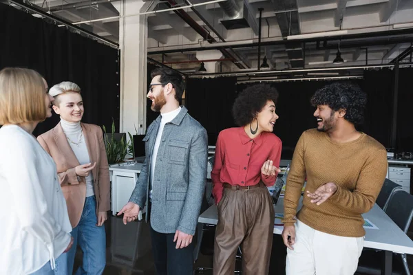 Alegre gente de negocios multiétnicos hablando y haciendo gestos en la agencia de publicidad - foto de stock