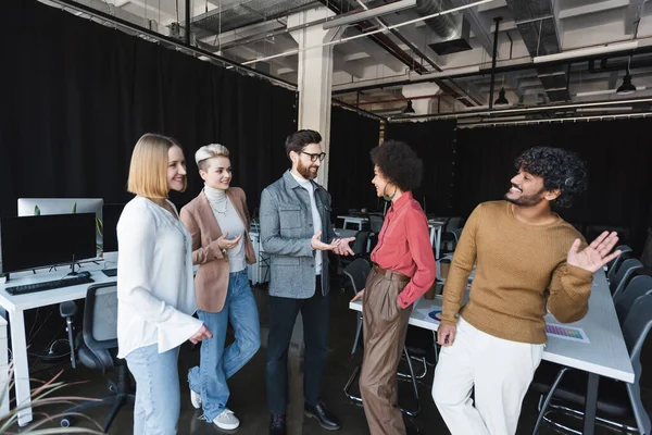 Hombre indio feliz saludando mano cerca de colegas multiétnicos en la agencia de publicidad - foto de stock